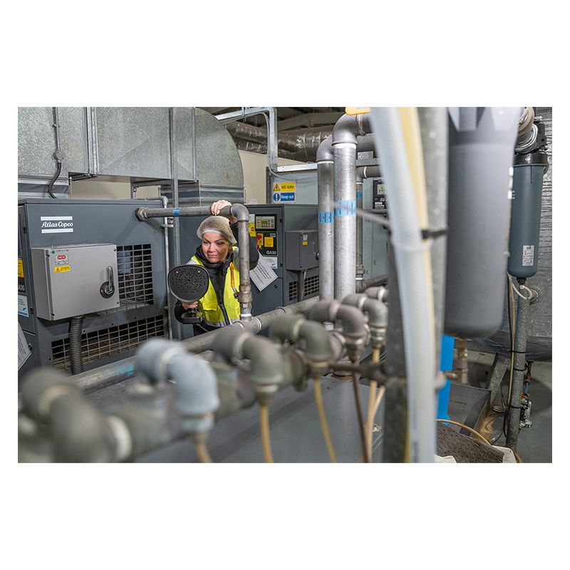 A woman is inspecting mechanical equipment using a FLIR Si1-LD Acoustic Camera